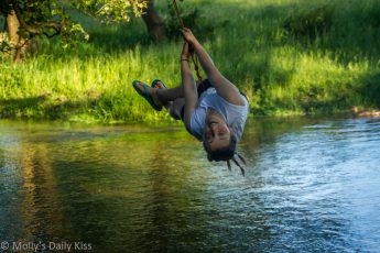 Child on rope swing over river having fun