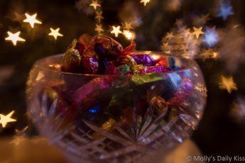 Quality Street chocolates in a bowl with Christmas tree bokeh lights