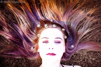 Young girl with hair splayed out around her with flowers in her hair and multi coloured hair