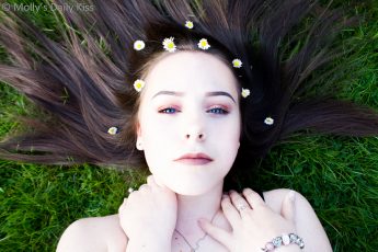 Girl laying on grass with flowers in her hair and blue eyes. Secrets in her eyes