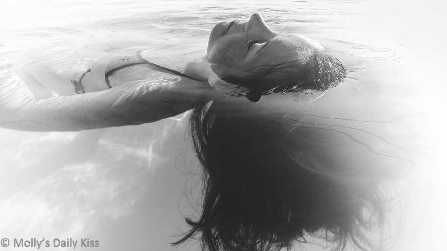 Undine, girl floating in water on her back with hair swirling round her head in black and white