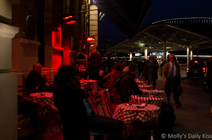 People sitting outside under heat lamps at Kings Cross station in London