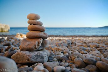 tower of pebbles on the beach with blue ocean in the background. Elemental