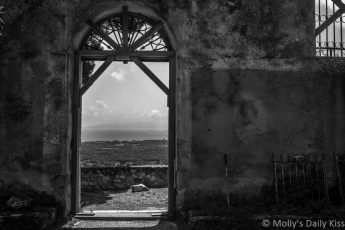 Abandoned church in Kefalonia greece, looking out through the door at the view beyond edited in black and white