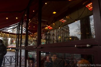 reflections of lights and other buildings in the window of a paris cafe