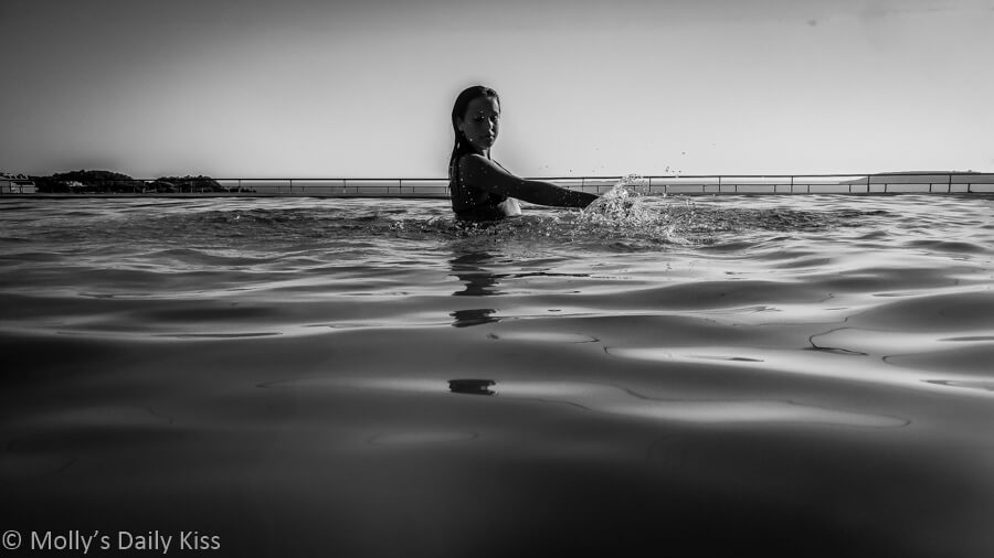 Girl in swimming pool splaching the water in black and white