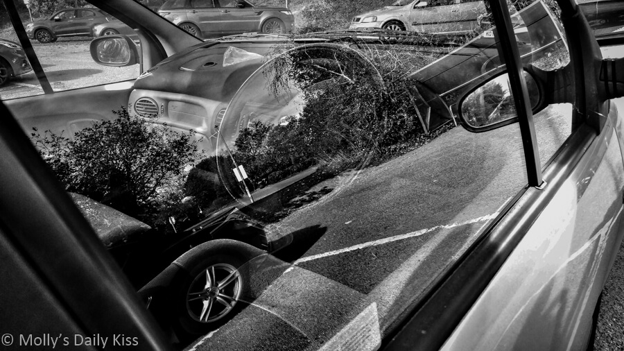 reflection of trees and other car in the window of a car in black and white