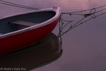 reflection of red rowing boat hull in the water which is the boats support