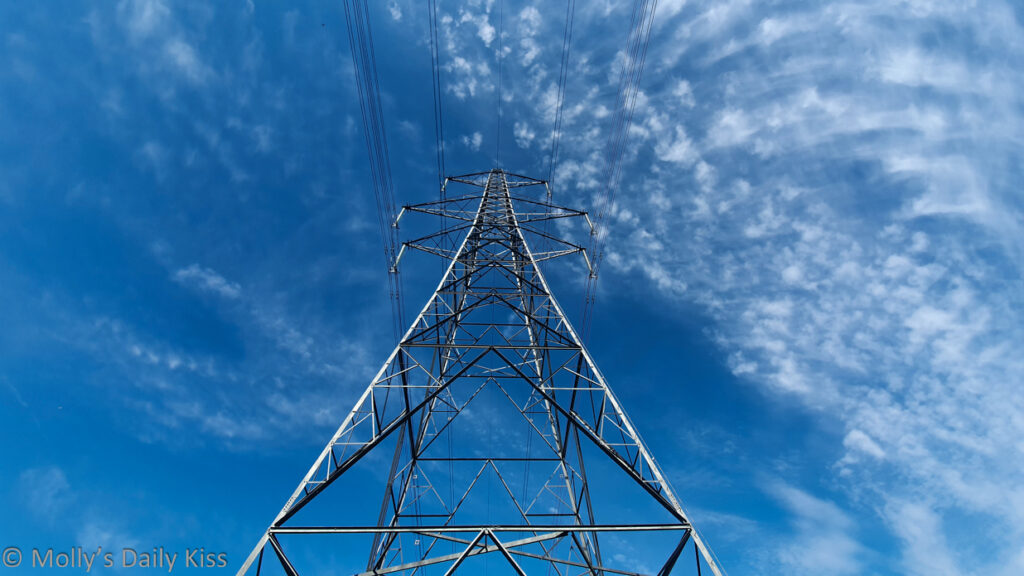 Looking up at electricity pylon against blue sky with wispy white clouds