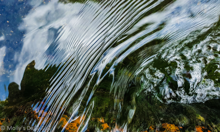 Sky reflected in water next to ripples over a rock