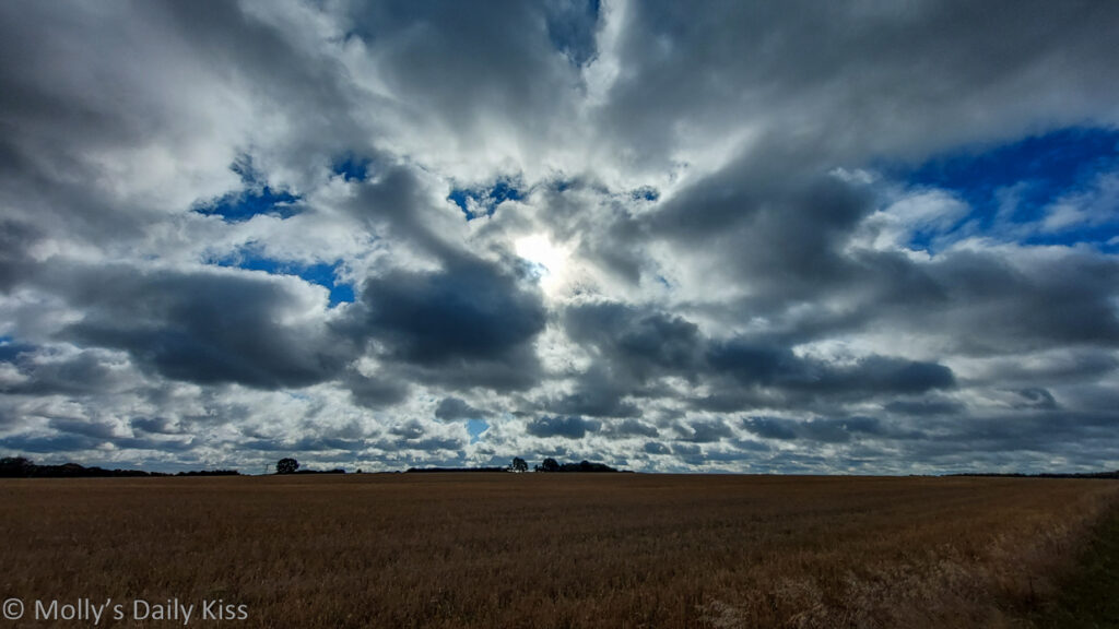 Sun shining through broken clouds over fields
