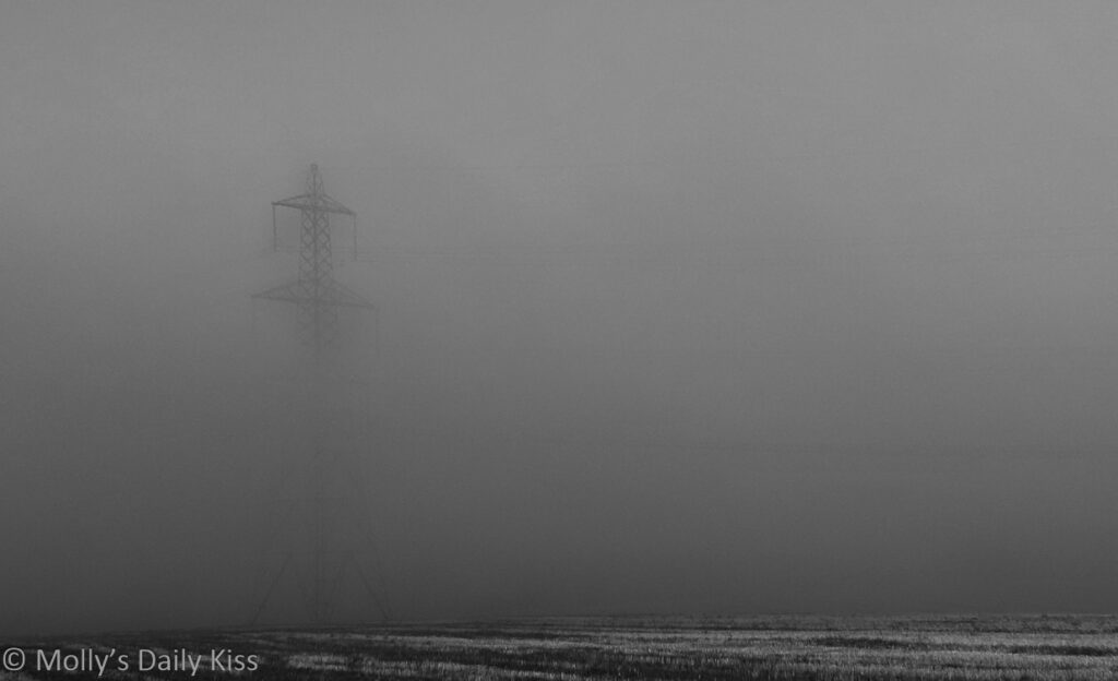 eerie electricity pylon showing through winter mist