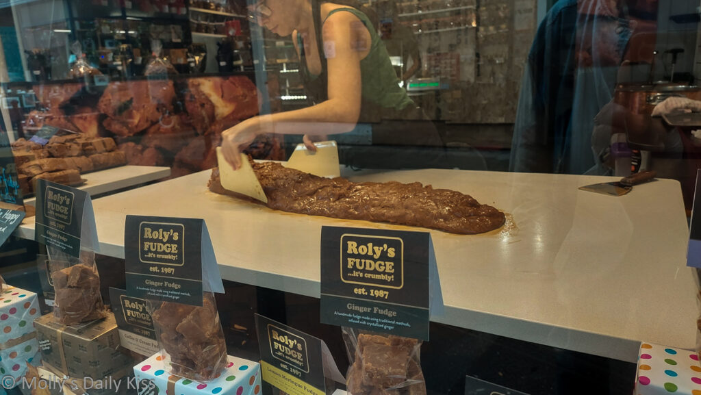 Woman making fudge in shop window with reflections of the street outside
